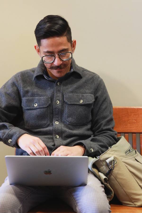 A CBU graduate student working on a laptop while sitting on a bench in a hallway.